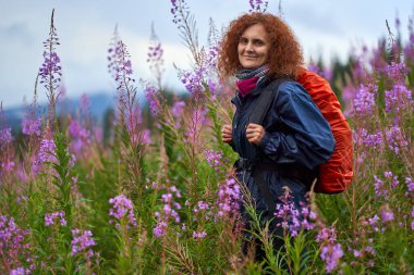 Yağmurlu bir günde sırt çantalı bir kadın dağ çiçekleri tarlasında yürüyüş yapıyor.