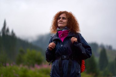 Sırt çantalı Kafkas kadın yağmurlu bir günde dağlarda yürüyüş yapıyor.