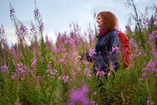 山の花のフィールドを介して雨の日にバックパックハイキングを持つ女性 — ストック写真