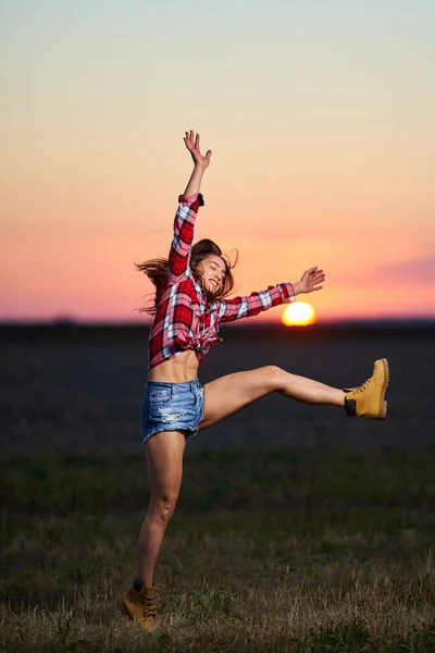 再生シャツと短いジーンズで若い農家の女性がフィールドで日没で喜びのためにジャンプ — ストック写真