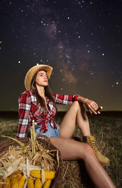 在星空下 穿着帽子 格子呢衬衫和短裤 头戴玉米篮的农民妇女 银河是可见的 — 图库照片