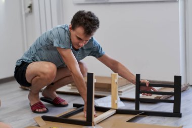 Genç adam yeni evinde mobilya montajı yapıyor, yeni hayat konsepti.