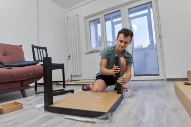 Genç adam yeni evinde mobilya montajı yapıyor, yeni hayat konsepti.