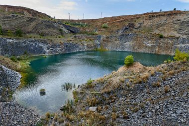 Eski bir taş ocağında oluşmuş bir göl manzarası tortulu kayalar ve görülebilir jeolojik katmanlar.