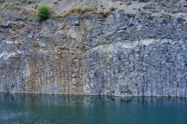 Eski bir taş ocağında oluşmuş bir göl manzarası tortulu kayalar ve görülebilir jeolojik katmanlar.