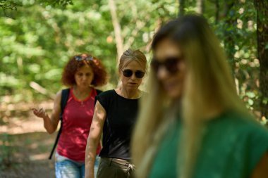 Üç kadın park yolunda birlikte ağaçlarla çevrili, açık havada yürüyüş yapıyorlar.