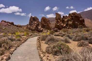 Volkanik yürüyüş yolu Roques de Garcia yakınlarındaki kayalık arazide Pico del Teide ile birlikte mavi bir gökyüzünün altında dönüyor.