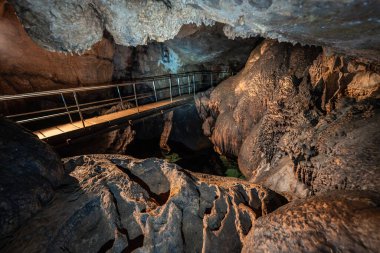 Metal bridge with railing inside a cave above eroded rock and underground river