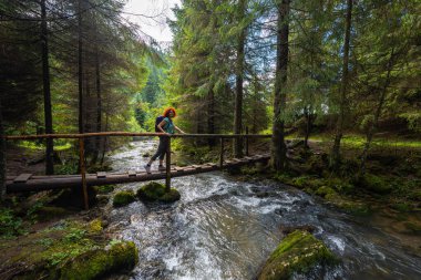Active female hiker with backpack crossing a wooden bridge over Ponor creek in Apuseni National Park, Romania, a scenic outdoor travel destination