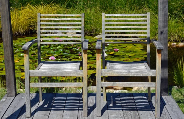 Wooden chairs on dock with lily pad pond in background