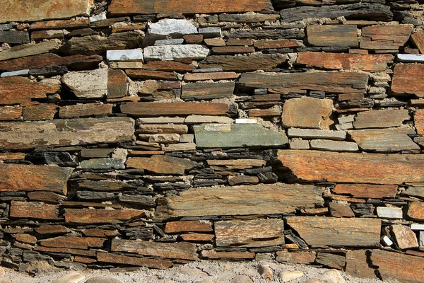 Wall built up of neatly laid out layers of flat stone blocks with various lengths and thicknesses.