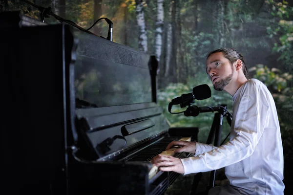 Young handsome bearded man playing piano and singing on forest background