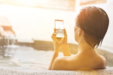 Asyalı Olgun kadın kaplıca havuzu cep telefonu kullanarak dikiz