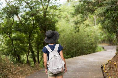 Bir Asyalı kadın dışarıda sırt çantasıyla yürüyüş yapıyor.