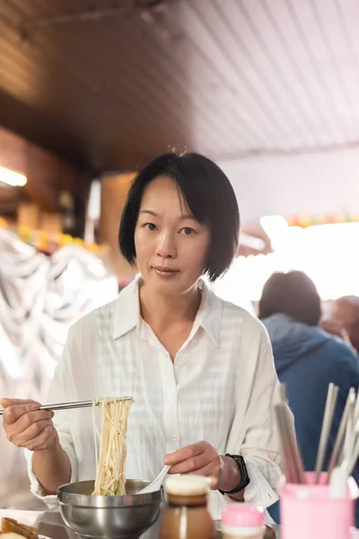 Зрелая азиатка ест лапшу — стоковое фото