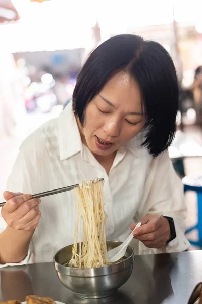 Зрелая азиатка ест лапшу — стоковое фото