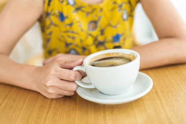 Kobieta trzymać filiżankę kawy na stole — Zdjęcie stockowe