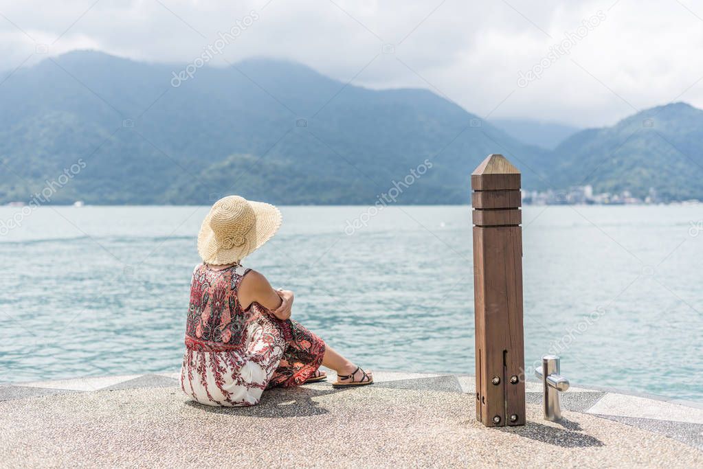 woman with hat sit at a pier