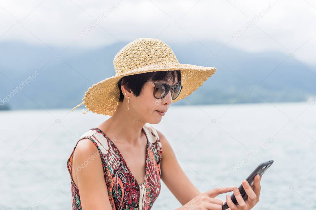 woman with hat sit at a pier using cellphone