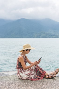 şapka ile kadın cep telefonu kullanarak bir iskelede oturmak