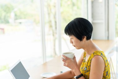 Kahvede çalışan ve laptop kullanan Asyalı bir kadın.