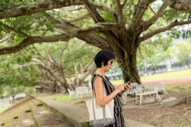Yetişkin Asyalı kadın merdivenlerde durur ve cep telefonu kullanır.