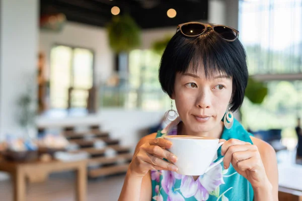 アジア系の熟女さんがお店でコーヒーを飲みながら — ストック写真