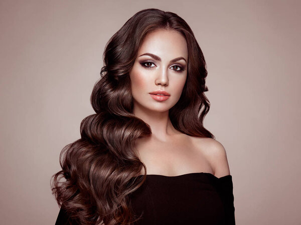 Брюнетка с длинными здоровыми и блестящими вьющимися волосами. Уход и красота. Образцовая женщина с волнистым хайрстиком. Макияж и черное платье