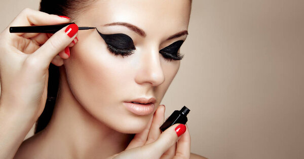 Makeup Artist Applies Eyeshadow. Beautiful Woman Make-up Eye with Black Liner. Fashion Makeup Arrows. Red Nails Perfect Skin