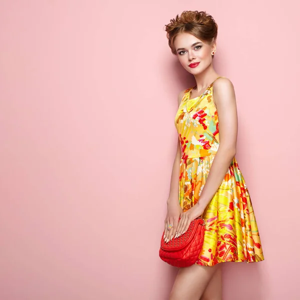花柄のドレスのファッションの若い女性の肖像画 スタイリッシュな春夏の服装で女性モデル ピンクの背景のポーズの女の子 スタイリッシュな髪型 赤いハンドバッグを持つ金髪の女性 — ストック写真