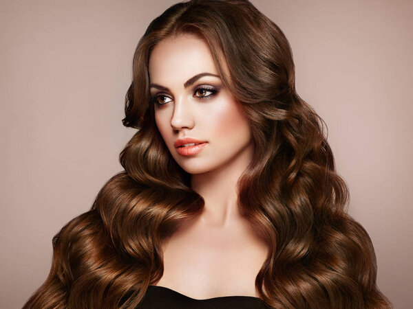 Брюнетка с длинными здоровыми и блестящими вьющимися волосами. Уход и красота. Образцовая женщина с волнистым хайрстиком. Макияж и черное платье