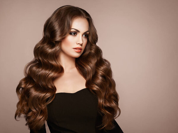 Брюнетка с длинными здоровыми и блестящими вьющимися волосами. Уход и красота. Образцовая женщина с волнистым хайрстиком. Макияж и черное платье