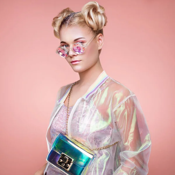 Holografik ceketli sarışın genç kadın. Bayan şık pembe gözlükler. Holografik folyo çanta ile model. Güzellik moda makyaj