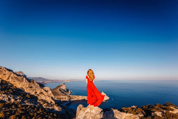 Jeune belle femme en robe rouge regardant vers la mer des montagnes — Photo