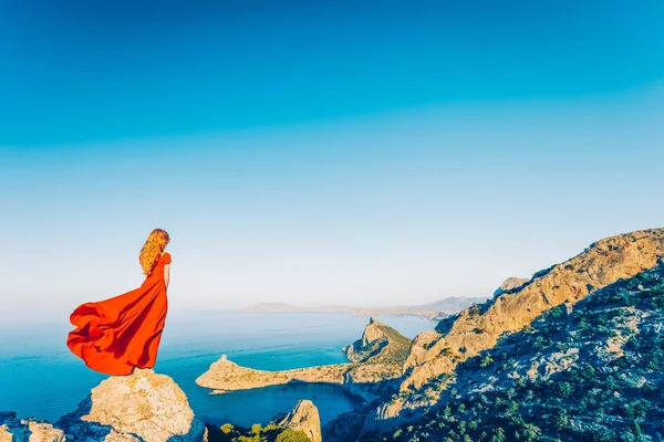 Jeune belle femme en robe rouge regardant vers la mer des montagnes — Photo