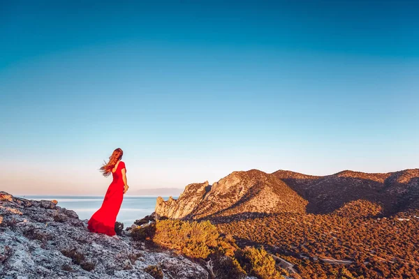 Jovem mulher bonita em vestido vermelho olhando para o mar montanhas — Fotografia de Stock