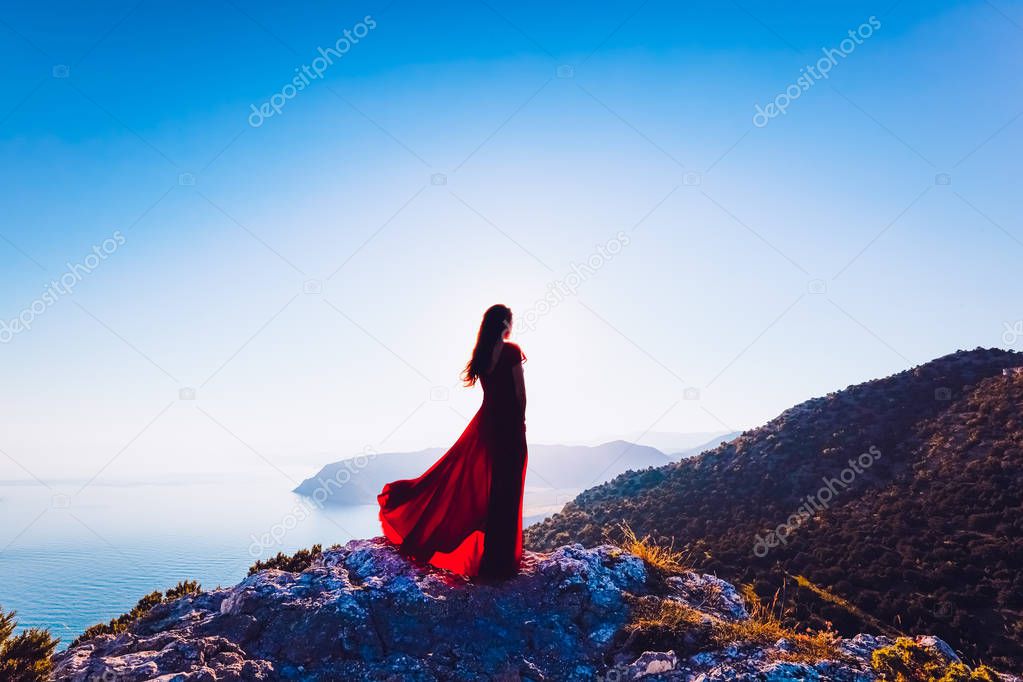 Young beautiful woman in red dress looking to mountains sea