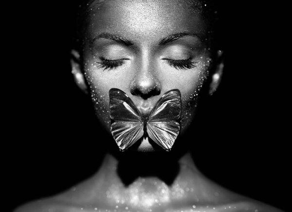 Fashion model woman in bright sparkles and lights posing in studio. Portrait of beautiful sexy woman with butterfly. Art design glitter glowing make up. Black and white photography