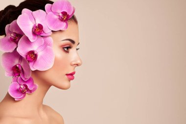 Orkideli güzel bir genç kadının portresi. Lüks makyajlı esmer kadın. Mükemmel cilt. Kirpiklerim. Kozmetik göz farı. Mor çiçekler.