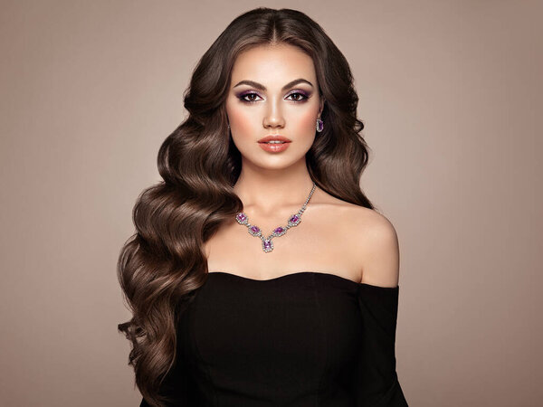 Брюнетка с длинными здоровыми и блестящими вьющимися волосами. Уход и красота. Образцовая женщина с волнистым хайрстиком. Макияж и ювелирные изделия
