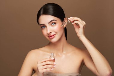 Genç ve güzel bir kadın pipetle yüz serumu uyguluyor. Yüz bakımı için estetik prosedürler