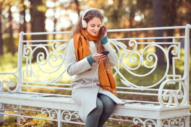 Genç kızıl saçlı bir kadın sonbahar parkında bir bankta oturuyor. Sonbahar ormanlarında müzik dinleyen bir kız.