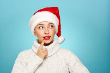 Beyaz örgü süveter ve mavi arka planda izole edilmiş Noel Baba şapkası giyen güzel bir kadın. Noel ya da yeni yıl şenlikleri. Tatil ve Parti