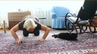 Yaşlı bir kadın egzersizleri yapıyor ve bir kedi ile oynarken