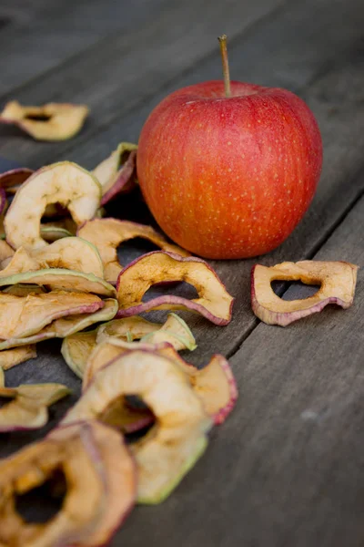 Целое яблоко и горсть сушеных яблочных ломтиков на столе — стоковое фото