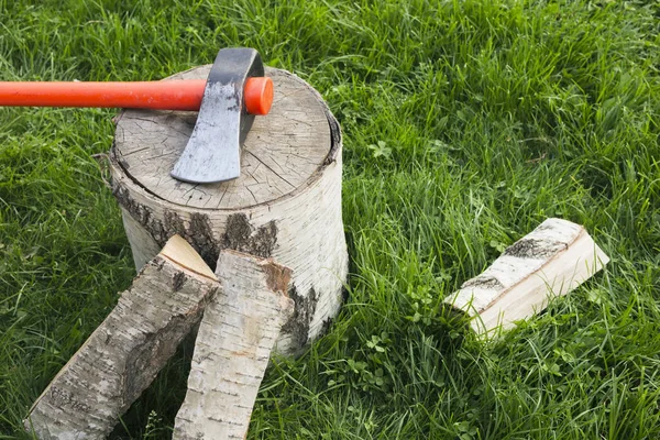 Stump com um machado de divisão e lenha na grama — Fotografia de Stock