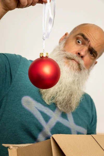 Homem barbudo olhando para bola de Natal vermelho — Fotografia de Stock