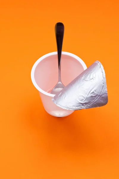 Порожня чиста чашка йогурту з ложкою на помаранчевому фоні — стокове фото