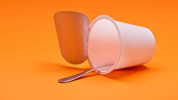 Empty clean yogurt cup with spoon on an orange background — Stock Photo, Image