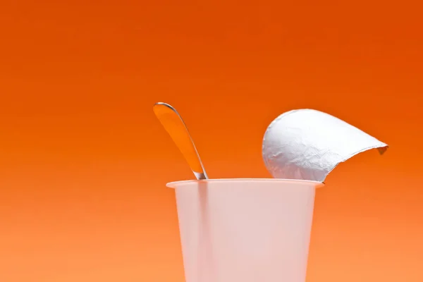 Copo de iogurte limpo vazio com colher em um fundo laranja — Fotografia de Stock